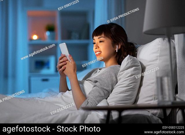 woman with phone and earphones in bed at night