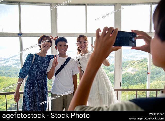 A boy using his mobile phone to take a picture of three people, a 13 year old boy, his mother and a friend