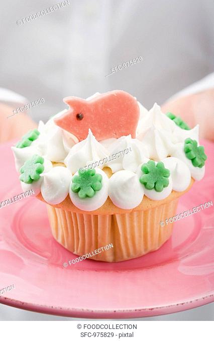 Hands holding cupcake with marzipan pig on pink plate