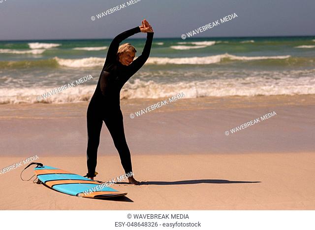 Front view of senior female surfer with surfboard exercising on the beach