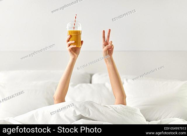 hands of woman lying in bed with cup of juice