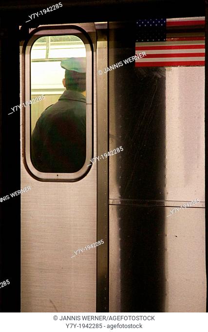 Back of an NYPD police officer seen through the window on an MTA subway car, with the car's US flag sticker next to him