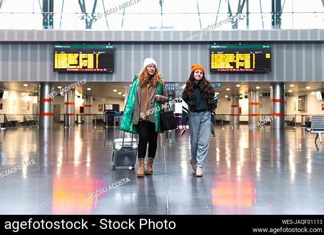Woman and daughter with suitcase walking at train station