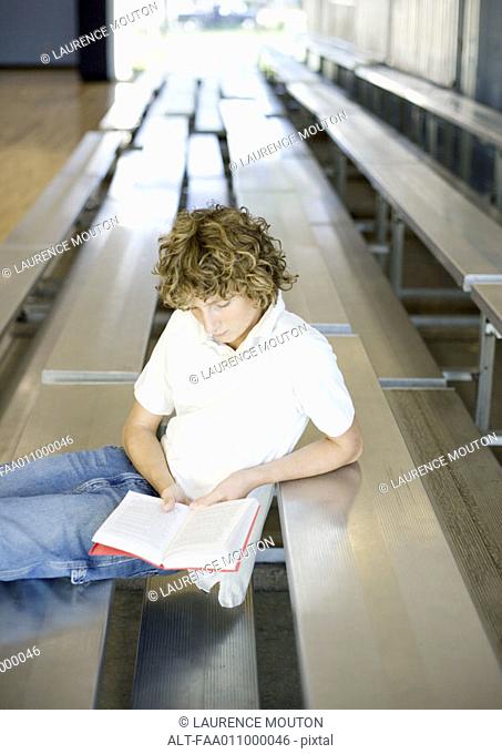 Teen boy reading book on bleachers