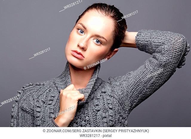 Beauty portrait of young woman in gray wool sweater. Brunette girl with bright blue eyes and day female makeup