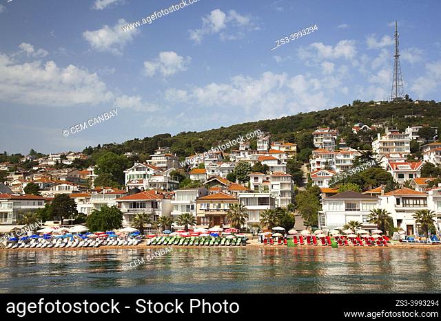View to the traditional houses in Kinaliada island with the colorful sunbeds and parasols in the foreground at the beach, Princes' Islands, Istanbul