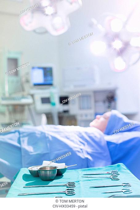 Surgical scissors and equipment on tray near female patient in operating room
