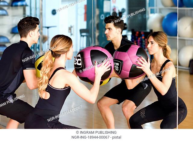 Man and Woman lifting fitballs in the gym. Young people wearing sportswear clothes in front of a mirror