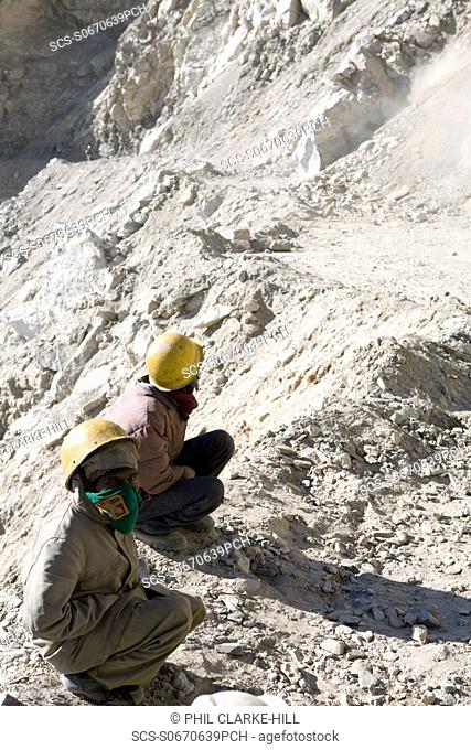 2 young male Indian road workers with hard hats on, looking at landslide on a mountain road, Nako - Tabo road, Spiti valley, Himachal Pradesh, Himalayas, India