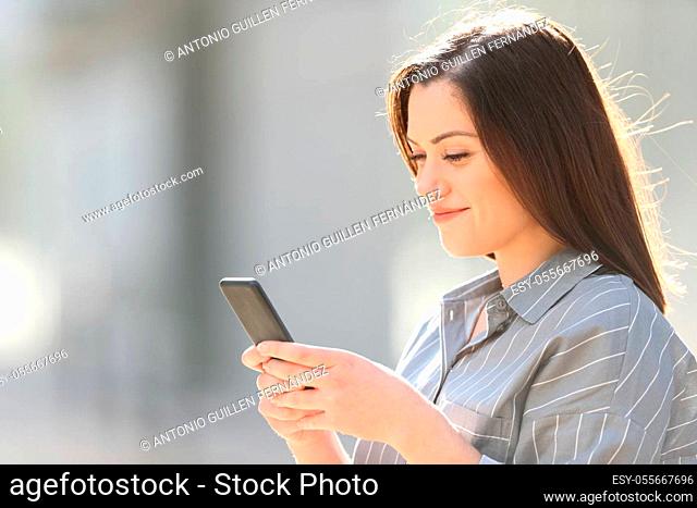 Satisfied woman using smart phone walking in a sunny street