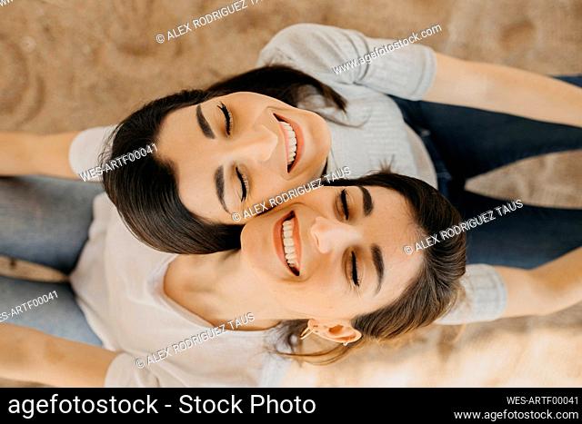 Smiling sisters with eyes closed on sand at beach