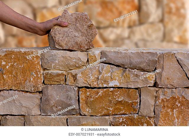 Mason hands working on masonry stone wall stonewall