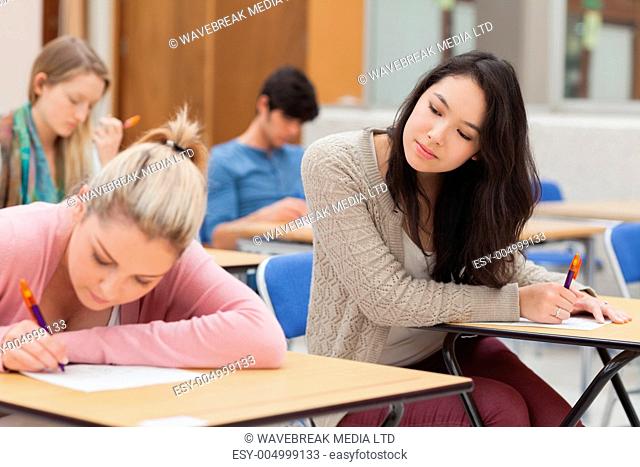 Girl copying another students work in exam i nexam hall in college