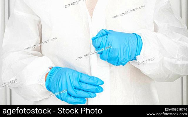 Closeup of female doctor of bacteriologist wearing and putting on protective biohazard suit, glasses, gloves and facial medical mask respirator against covid-19...
