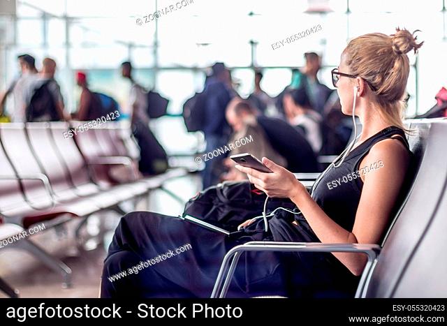 Casual sporty young blond female traveler talking on her cell phone while waiting to board a plane at the departure gates at the asian airport terminal