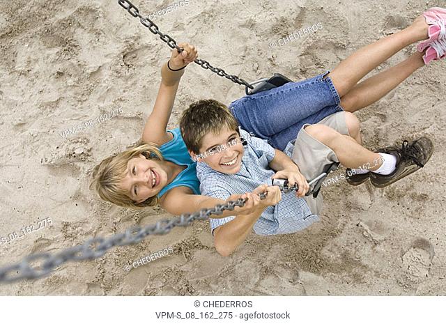 High angle view of a boy sitting on a swing and a teenage girl holding a mobile phone