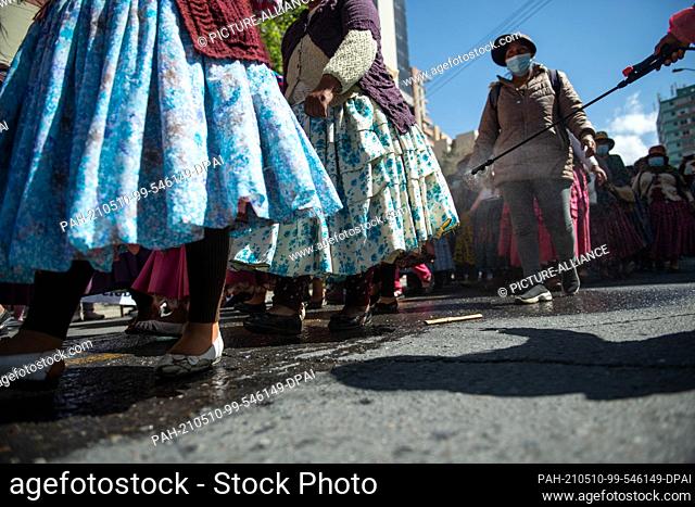 10 May 2021, Bolivia, La Paz: A person on the sidelines of a protest sprays demonstrators in traditional dress during a protest to demand better education...