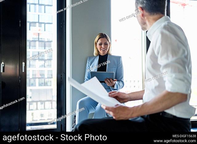 Smiling businesswoman using digital tablet while discussing with male colleague in office