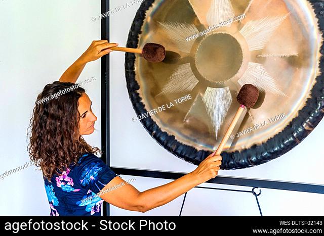 Female sound therapist playing gong with mallets in studio