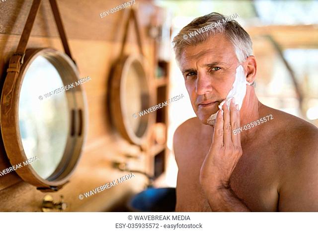 Man applying shaving cream on his face in cottage during safari vacation