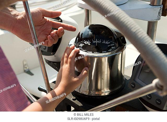 Father and son on board yacht, father pointing to speedometer