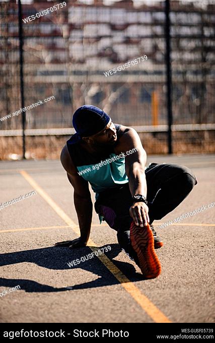 Young man stretching hand on basketball court during sunny day