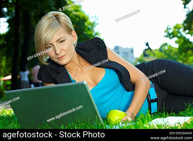 Young businesswoman lying in grass in park, using laptop computer