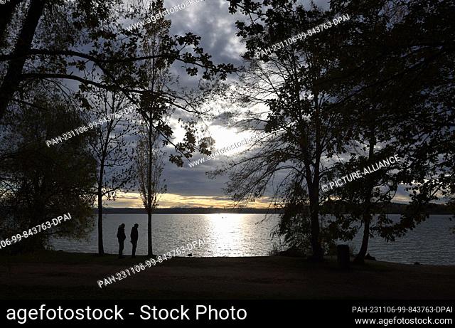 06 November 2023, Bavaria, Inning: Excursionists watch a duck on the shore of Lake Ammersee, glistening in the sunshine. Photo: Karl-Josef Hildenbrand/dpa