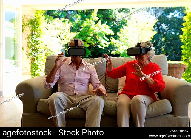 Senior caucasian couple sitting on sofa together wearing vr headset touching virtual screen