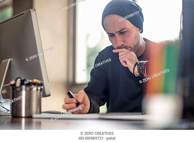 Young male designer contemplating at home desk