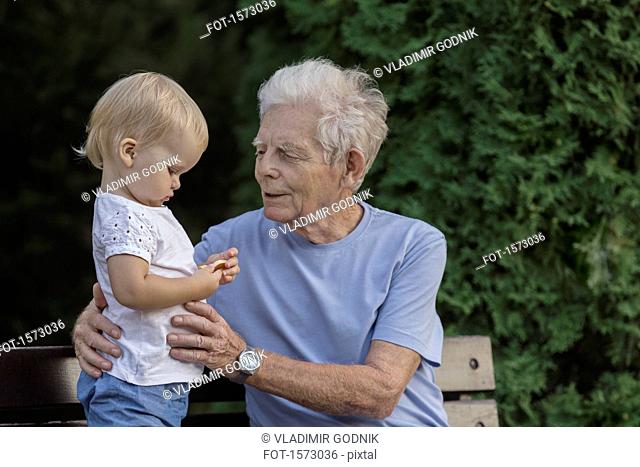 Smiling grandfather playing with girl on park bench