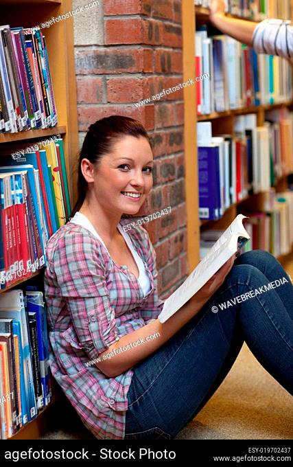 Smiling young woman reading a book sitting on the floor in a bookstore
