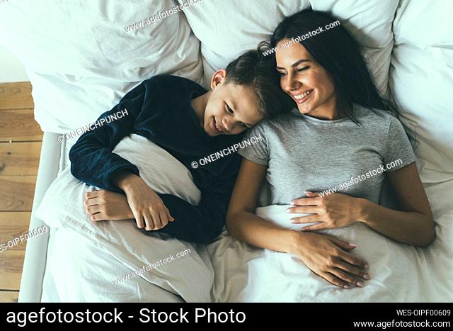 Smiling son and mother lying on bed at home