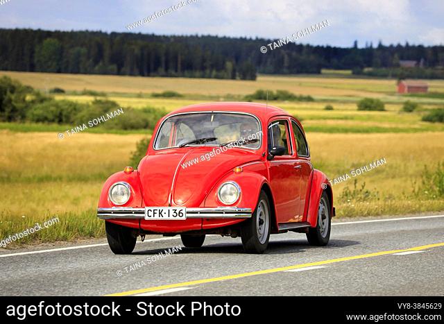 Red Volkswagen Beetle, officially Volkswagen Type 1, driving along country road on Maisemaruise 2019 car cruise. Vaulammi, Finland. August 3, 2019