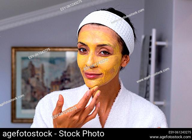 Portrait of caucasian young woman applying facial mask in bathroom