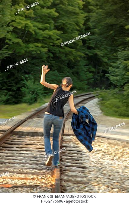 Stylized image of girl in jeans balancing on / walking on railroad tracks in New Hampshire, USA