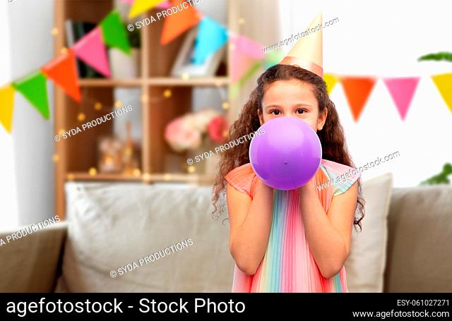 little girl in birthday party hat blowing balloon
