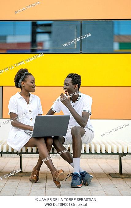 Young couple sitting on bench with laptop