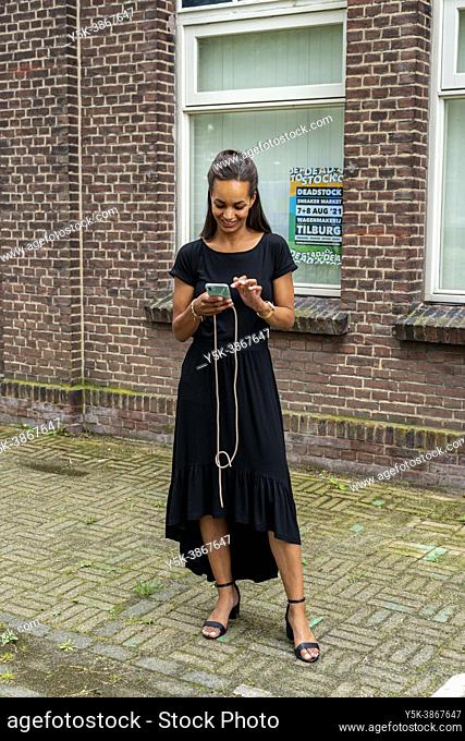 Tilburg, Netherlands. Young, coloured beautiful woman checking her smartphone messages with a happy smile