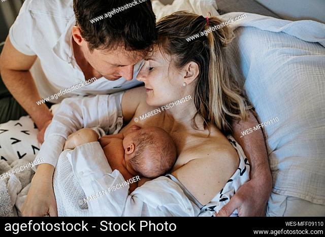 Father embracing woman and son lying on bed at home