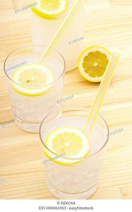 fresh lemonade drink with lemon slice closeup and pitcher carafe over pinewood table