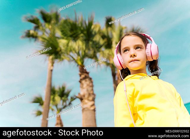 Portrait of serious little girl listening music with headphones outdoors
