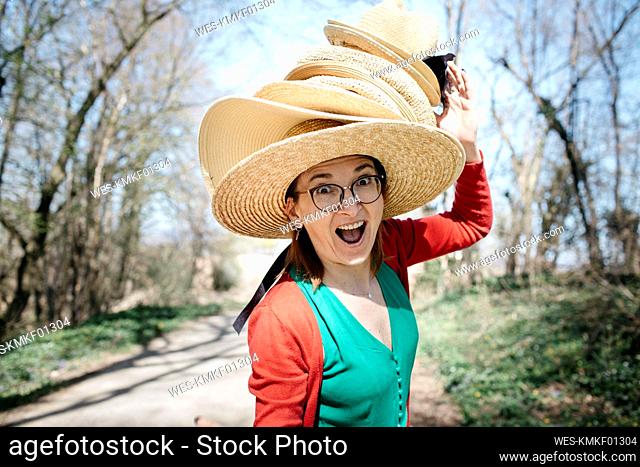 Portrait of mature woman with stack of straw hats on her head pulling funny faces