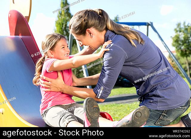 Woman and little girl chuting down slide at playground