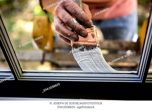 Close in detail of a 41 year old man painting the window trim of a house facing inside