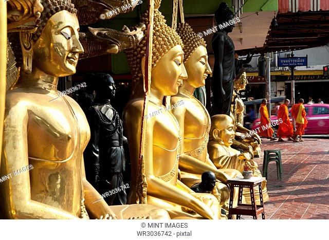 Tall golden Buddha statues lined up on a pavement
