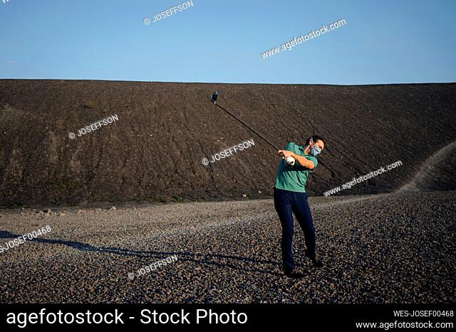 Mature man with a mask playing golf on a disused mine tip