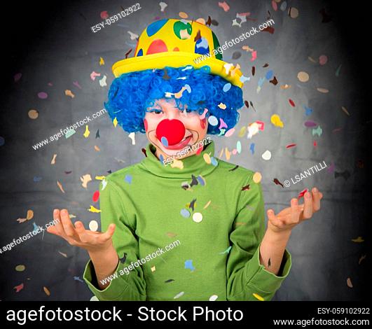 young child dressed as a clown with wig and fake nose has fun playing with colorful confetti celebrating carnival
