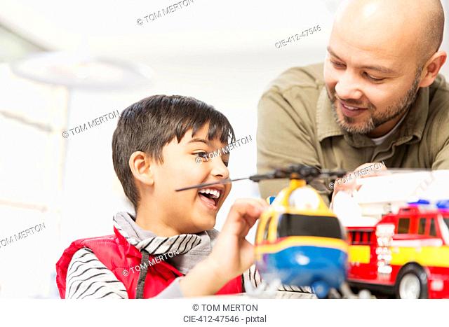 Father and son playing with helicopter and fire engine toys