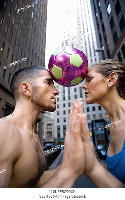Side profile of a young woman and a young man with a soccer ball between their heads
